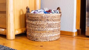 Una cesta de mimbre llena de ropa junto a un armario de madera y un televisor en la pared.