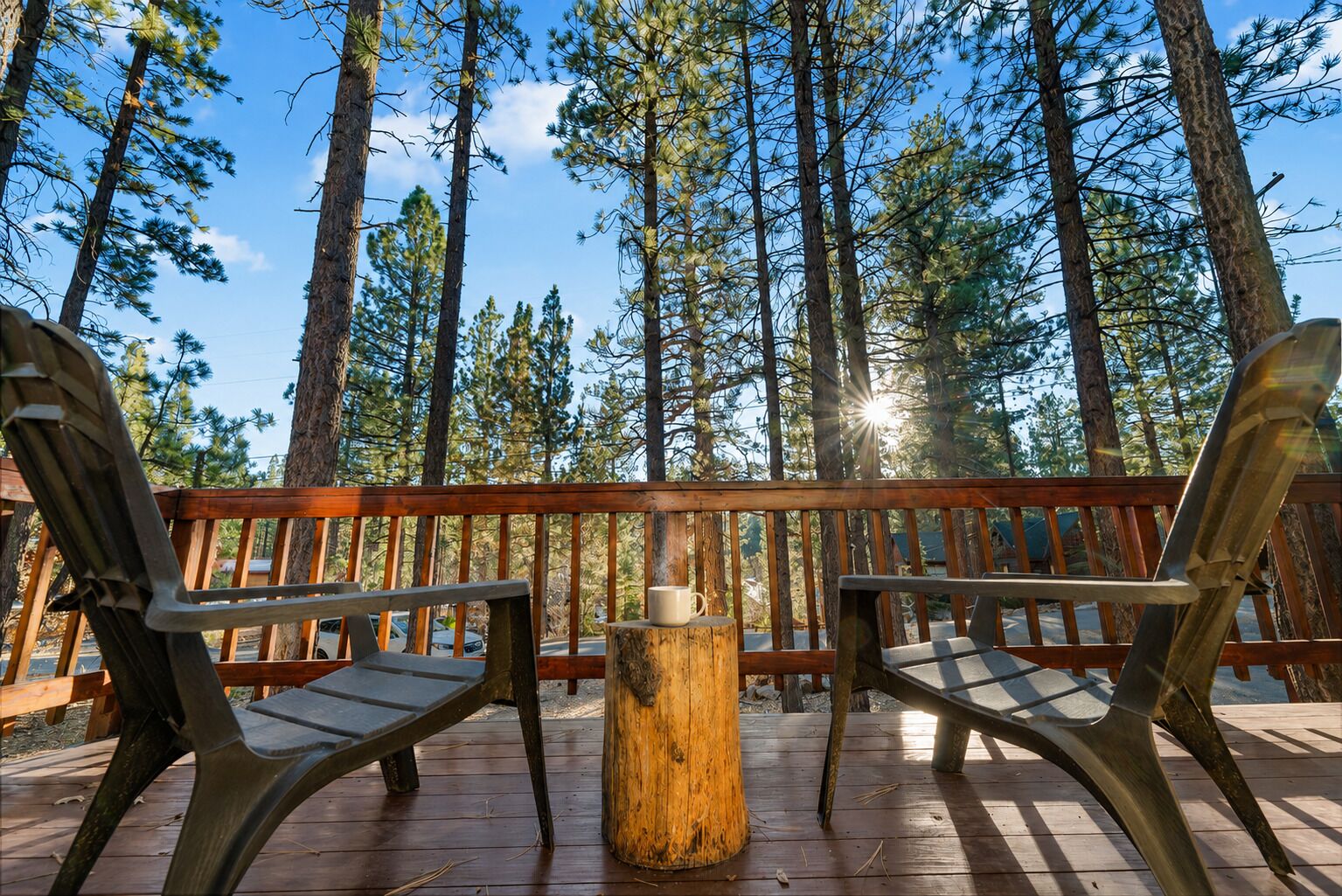 Una terraza de madera con dos sillas y una mesa central, rodeada de altos pinos.