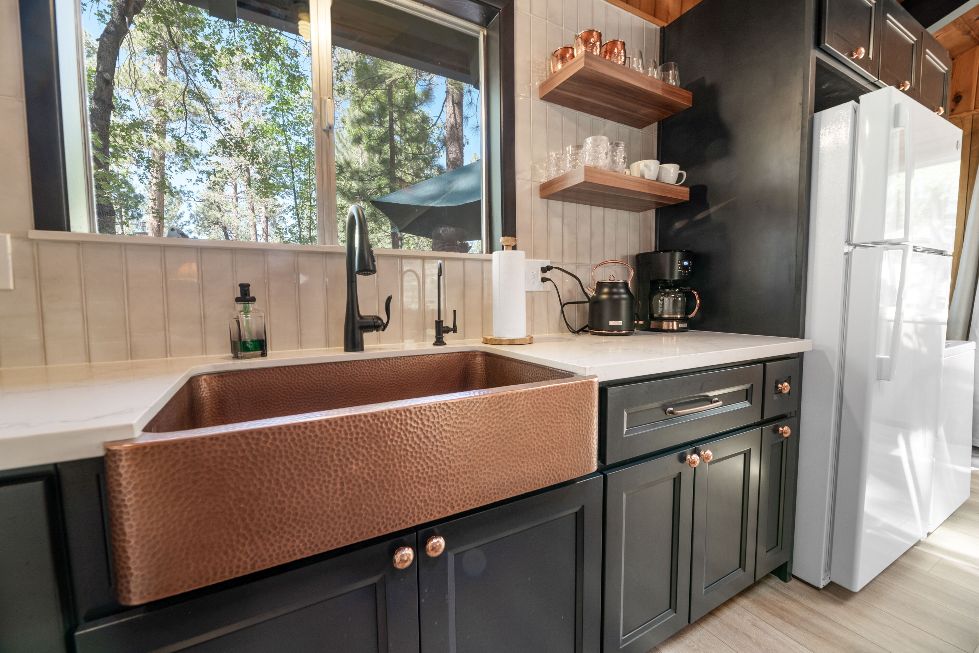 A modern kitchen with a copper sink, dark cabinets, and a white refrigerator.