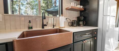 A modern kitchen with a copper sink, dark cabinets, and a white refrigerator.