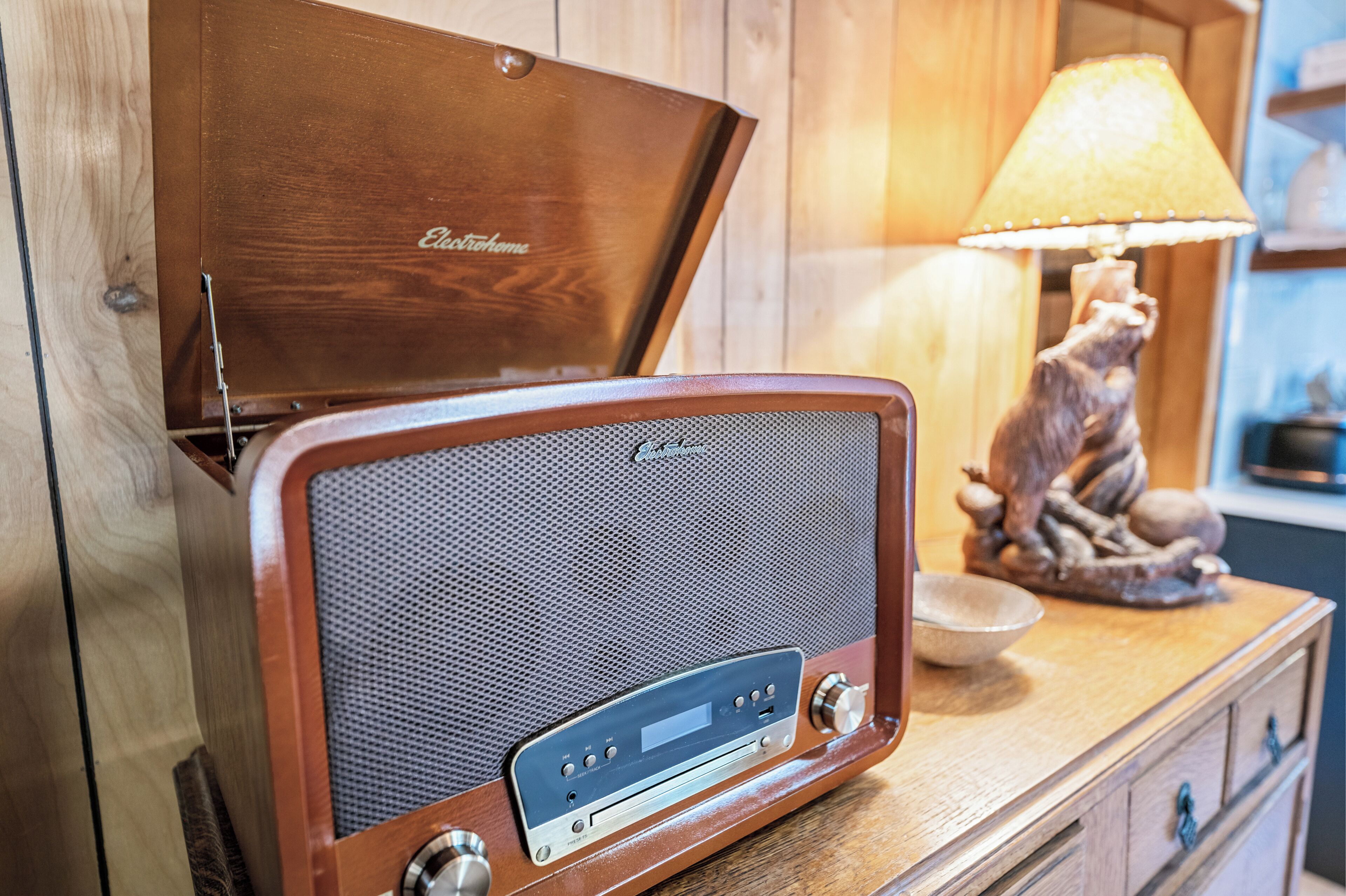 A vintage radio with a wooden cabinet, a decorative lamp, and a ceramic owl figurine on a wooden dresser.