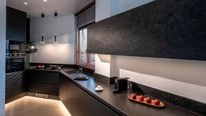 A modern kitchen with dark cabinetry, a built-in oven, and a sleek countertop. - Made By The Sea Villa 1 (Malevizi)