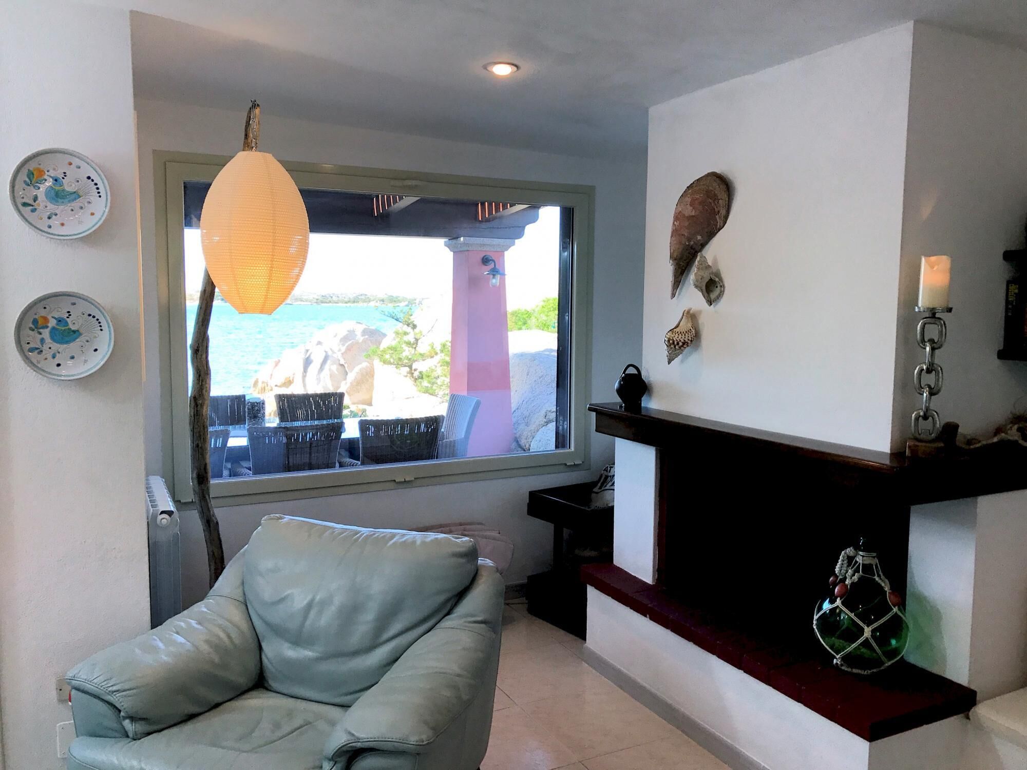 A living room with a view of the sea, a leather chair, a fireplace, and decorative plates on the wall.