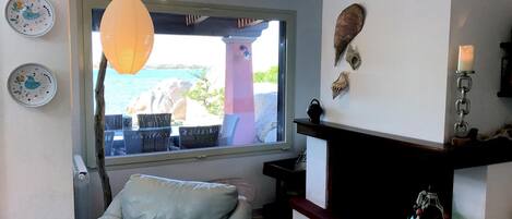 A living room with a view of the sea, a leather chair, a fireplace, and decorative plates on the wall.