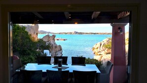 A dining area with a table and chairs, overlooking a coastal view with rocks and a body of water. - Villa Mica in La Maddalena (La Maddalena)