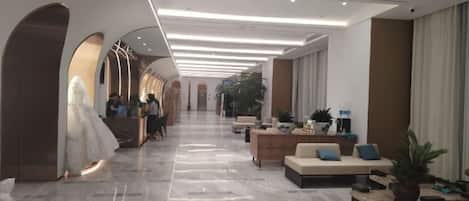 A hotel lobby with a long corridor, seating areas, and a reception desk.