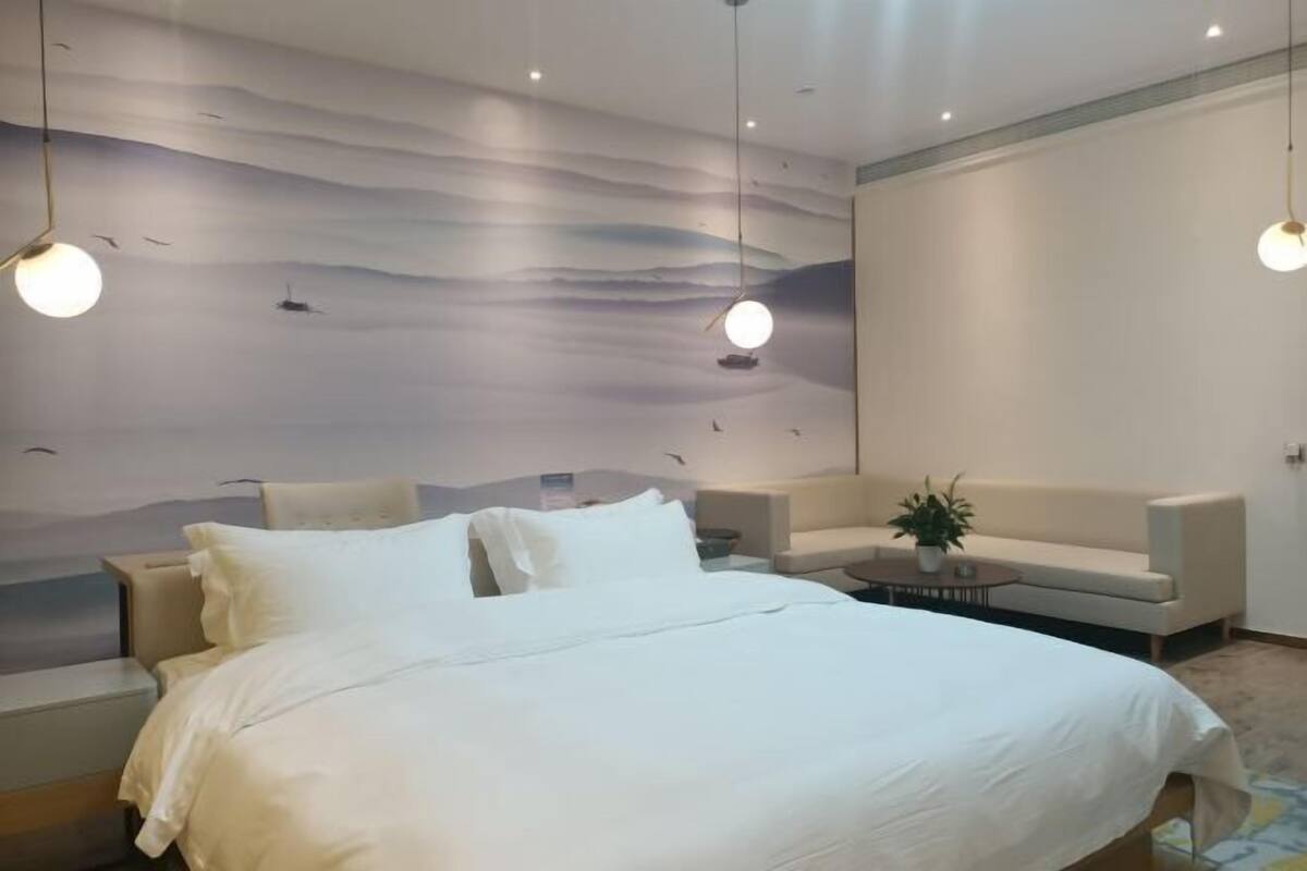 Relax in a serene space with a large bed, sofa, and unique wall mural featuring a peaceful landscape.