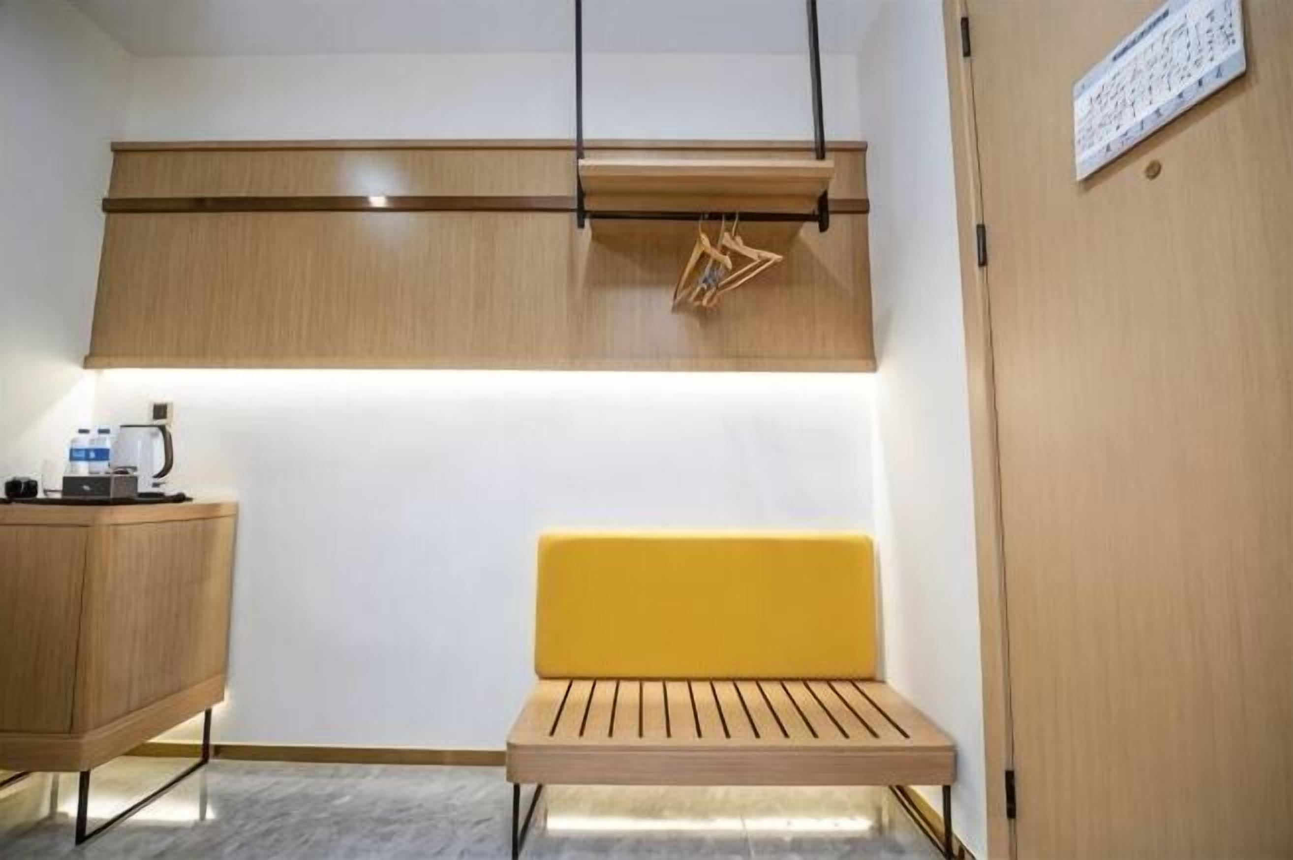 A compact room with a wooden bench, a small table with a kettle, and a cabinet.