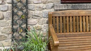 A stone wall with a wooden bench and a metal trellis with climbing plants. A window with a dark frame and a sign reading "5 WOODSIDE COTTAGE" is visible. - Woodside Cottage Grewelthorpe Nr Masham Ripon (Ripon)