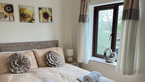 A bedroom with a large bed, two pillows, a window with curtains, and three wall-mounted sunflowers. - Woodside Cottage Grewelthorpe Nr Masham Ripon (Ripon)