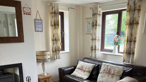 A living room with a sofa, a fireplace, a lamp, and curtains. - Woodside Cottage Grewelthorpe Nr Masham Ripon (Ripon)