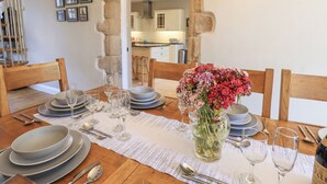 Una mesa de comedor dispuesta con platos, vasos, cubiertos, un florero con flores y una silla de madera.