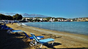 Una spiaggia con file di sedie a sdraio blu e vista libera sul mare e montagne lontane.