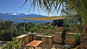 Patio esterno con tavolo e sedie, un muro in pietra e vista sulle montagne.