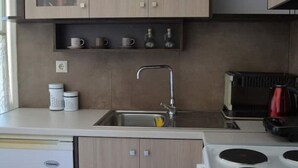 Una cucina compatta con mobili in legno chiaro, un lavello in acciaio inossidabile e un piano cottura bianco.