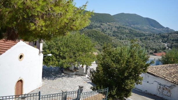 Un edificio bianco con una piccola finestra e un'entrata, circondato da alberi e un paesaggio montuoso sullo sfondo.