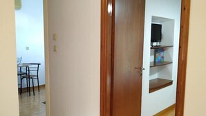 Un corridoio con una porta in legno, una sala da pranzo con tavolo e sedie, e uno scaffale con televisore.