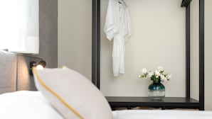 A neatly made bed with white bedding and a pillow, a bedside table with a vase of white flowers, and a white robe hanging on a black wall-mounted rack. - Villa LuiSole apartment °2 with heated saltwater pool, family-friendly, sea view (Krk)