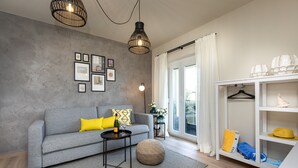 A modern living room with a grey sofa, round ottoman, black coffee table, and a white shelving unit with hats and bags. - Villa LuiSole apartment °2 with heated saltwater pool, family-friendly, sea view (Krk)