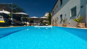 A clear blue swimming pool with lounge chairs and umbrellas, surrounded by a building with a white facade and windows. - Villa LuiSole apartment °2 with heated saltwater pool, family-friendly, sea view (Krk)
