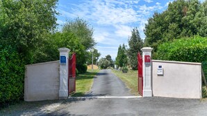A gated entrance with a clear path leading into a property surrounded by greenery. - Gîte in a holiday park with swimming pool (Saint-Savinien)