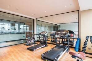 Un gimnasio moderno con equipo de cardio, máquinas de pesas y un espejo grande.