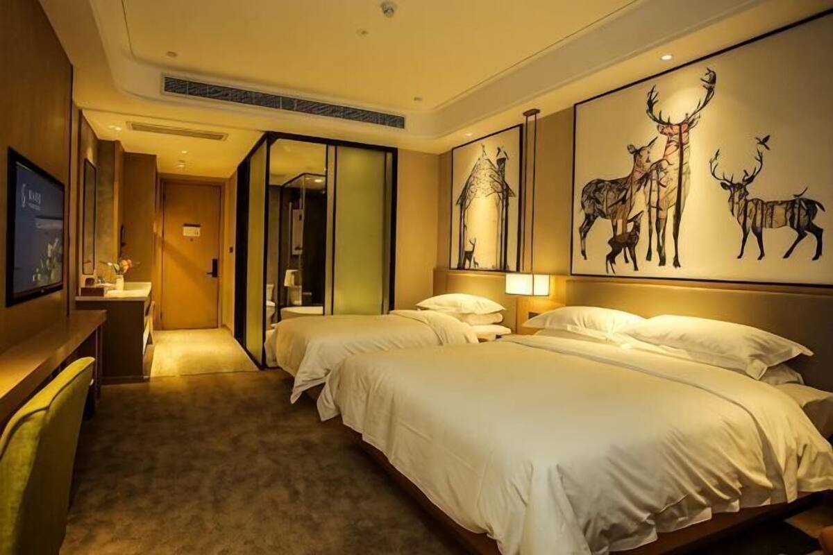 A hotel room with two beds, a desk, a mirror, and artwork on the wall.