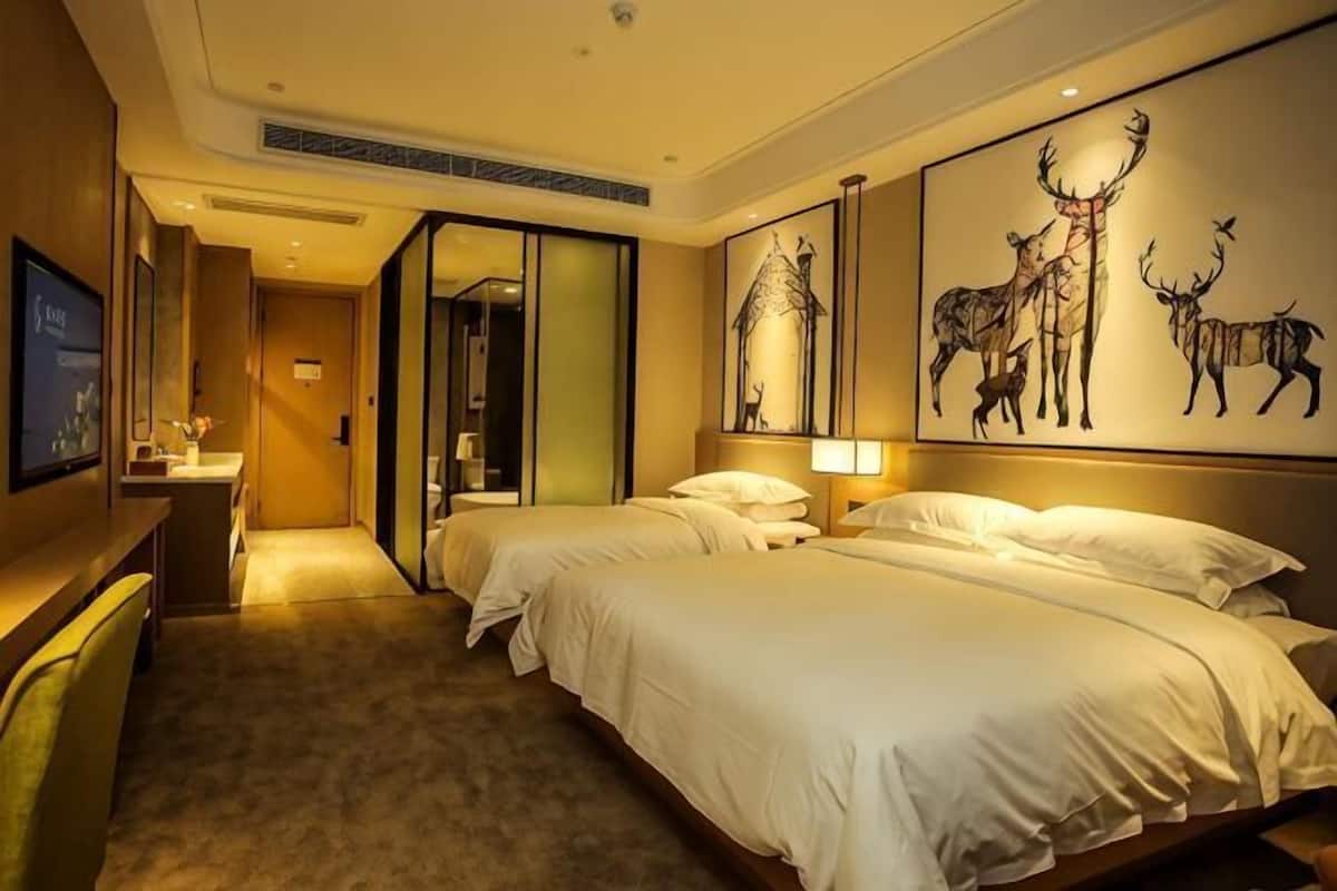 A hotel room with two beds, a desk, a mirror, and artwork on the wall.