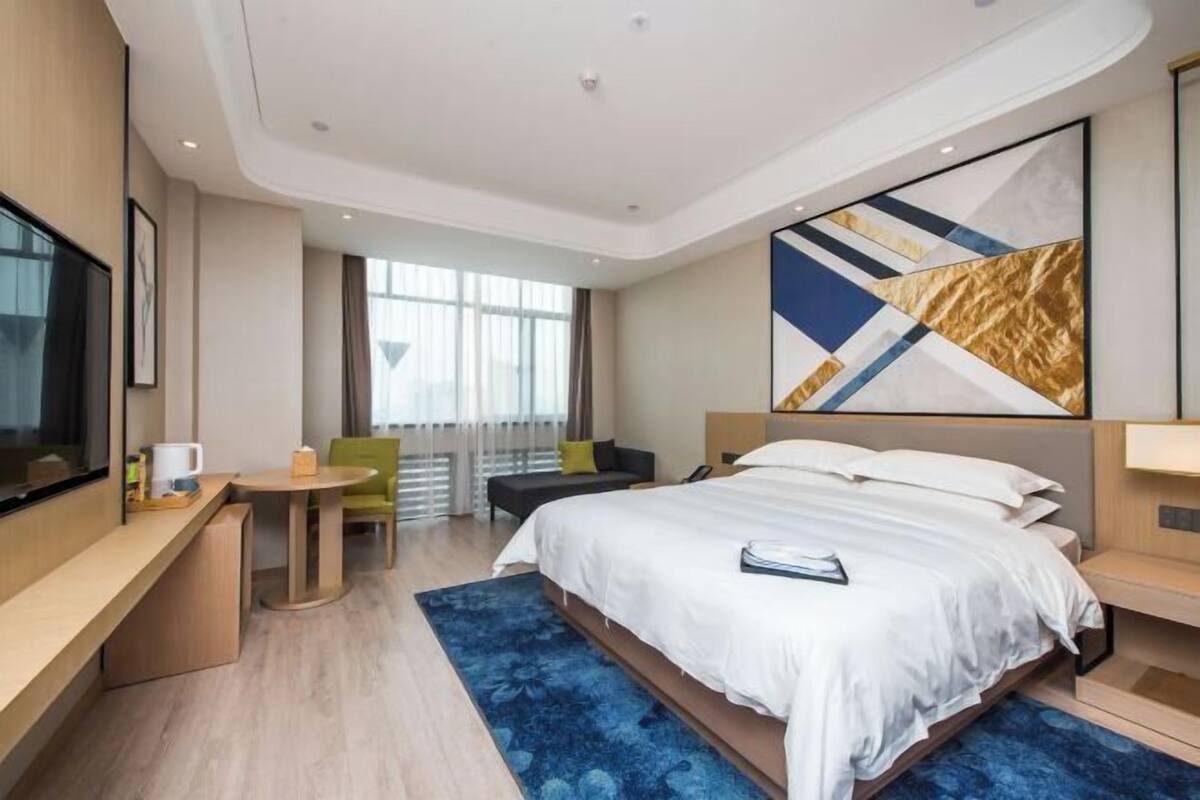 A modern hotel room with a large bed, a desk, a chair, and a TV.