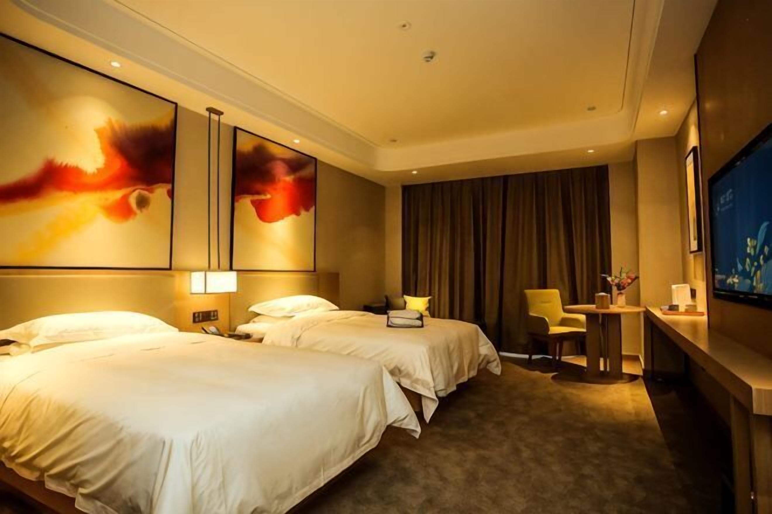 A hotel room with two beds, a desk, a chair, a television, and artwork on the walls.