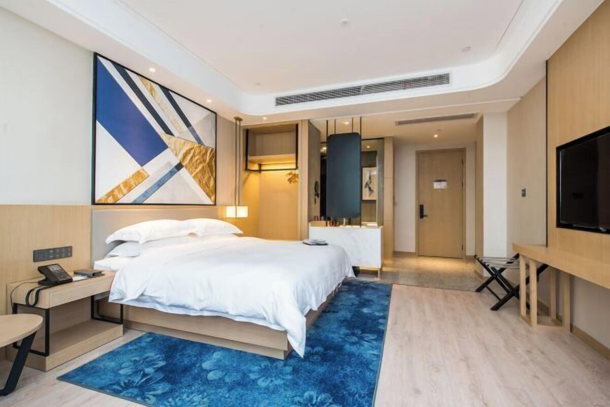 Una habitación de hotel moderna con una cama grande, mesitas de noche, un escritorio, un televisor de pantalla plana y un cuadro abstracto de grandes dimensiones en la pared.
