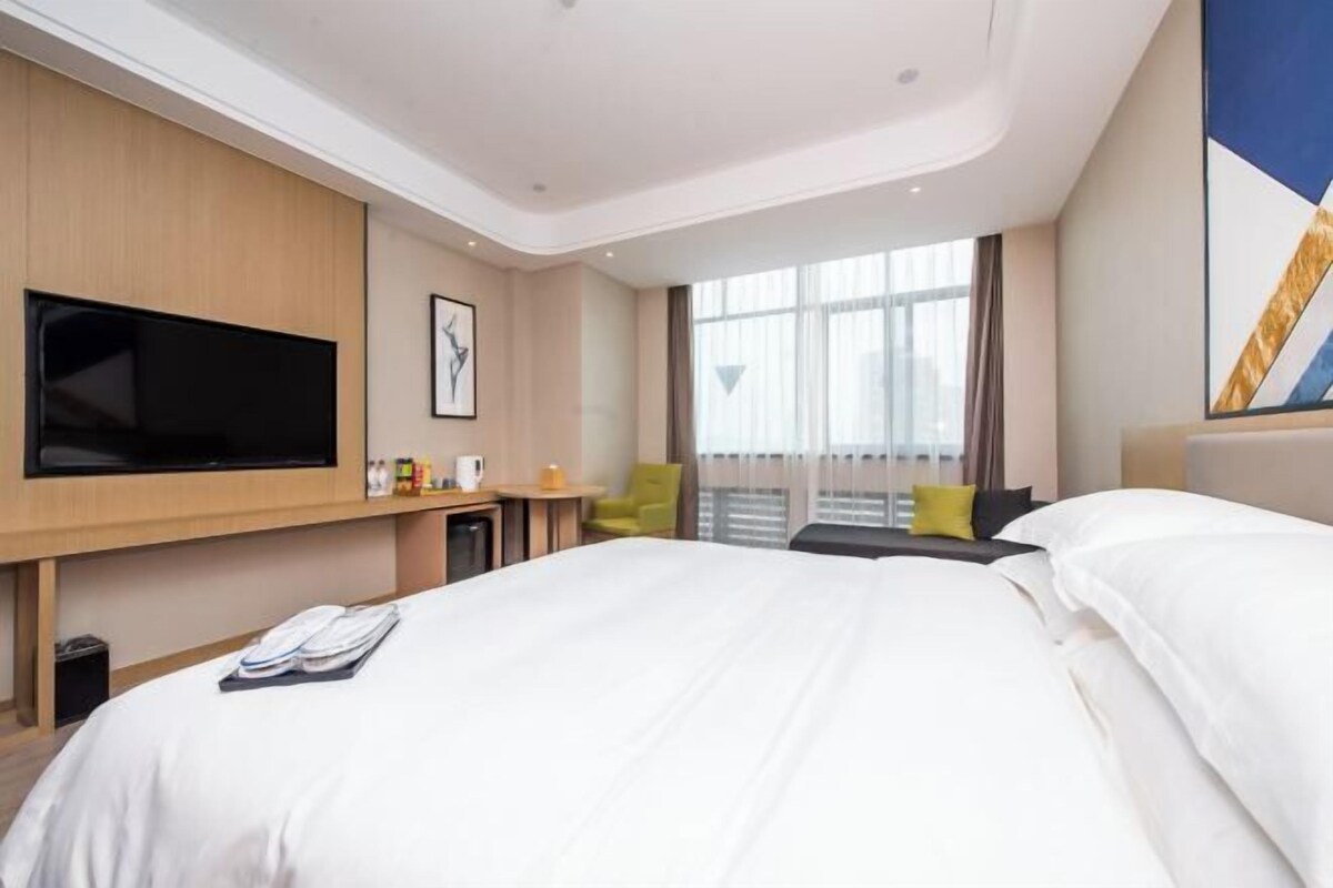 Habitación de hotel con una cama grande, un televisor de pantalla plana, un escritorio pequeño con una silla y un ventanal con cortinas.