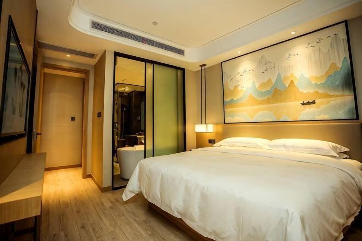A hotel room with a bed, a desk, a painting, and a sliding door leading to a bathroom.