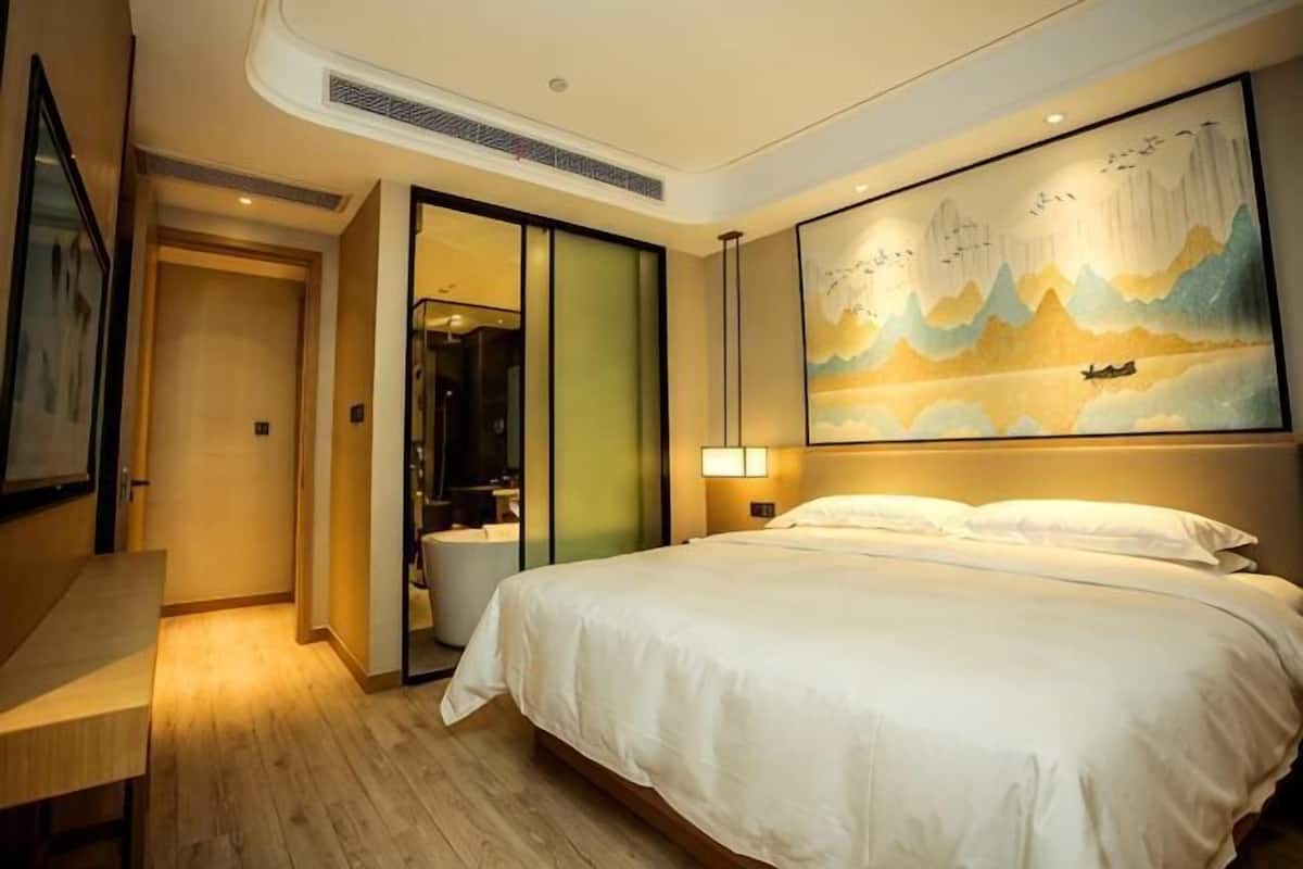 A hotel room with a bed, a desk, a painting, and a sliding door leading to a bathroom.