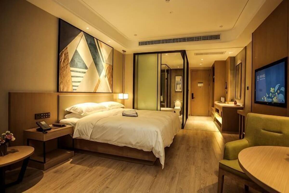 A hotel room with a bed, bedside table, lamp, TV, and a seating area.