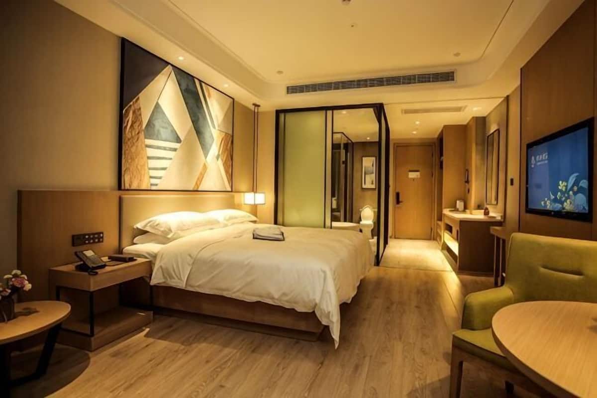 A hotel room with a bed, bedside table, lamp, TV, and a seating area.