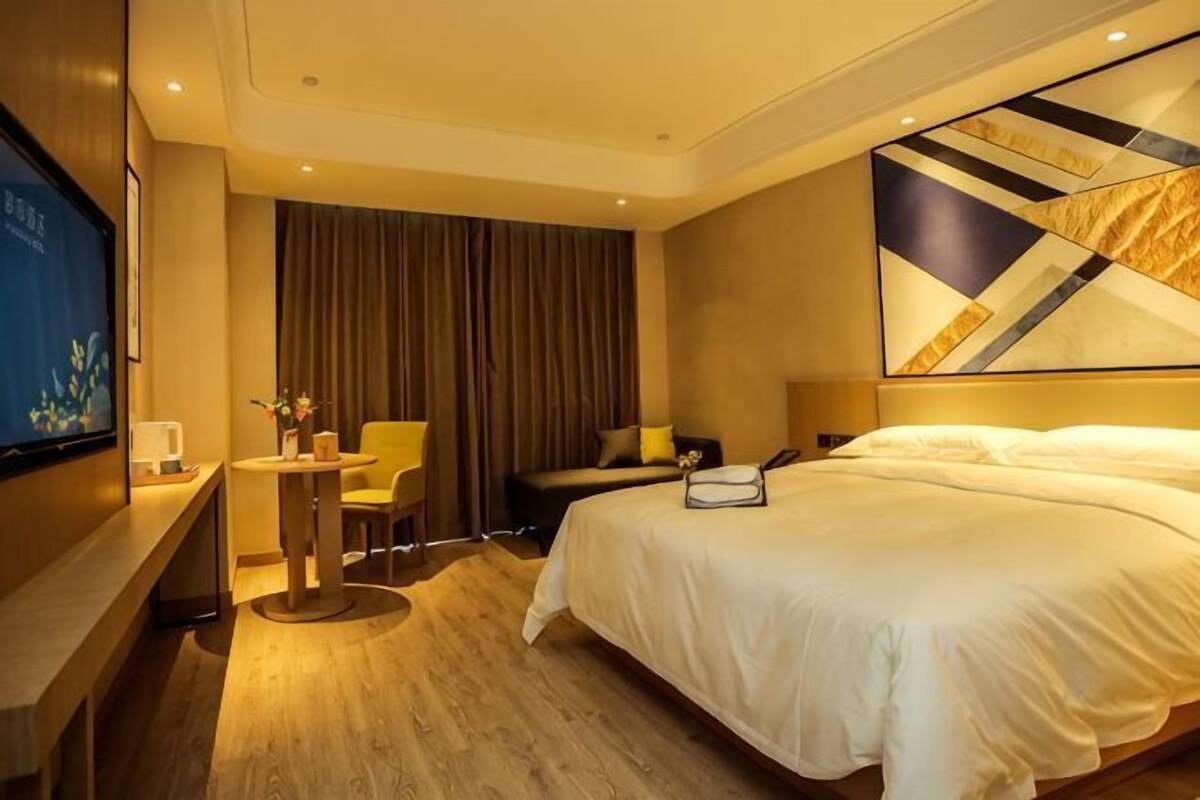 A hotel room with a bed, a desk, a chair, a TV, and a painting on the wall.