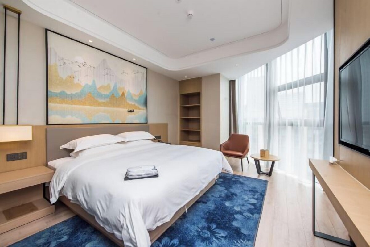 Una habitación de hotel moderna con una cama grande, televisión de pantalla plana, un cuadro en la pared y un ventanal amplio.