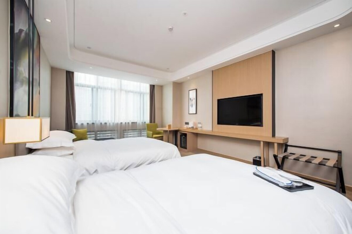 Habitación de hotel con dos camas, televisión, escritorio y ventana con cortinas.