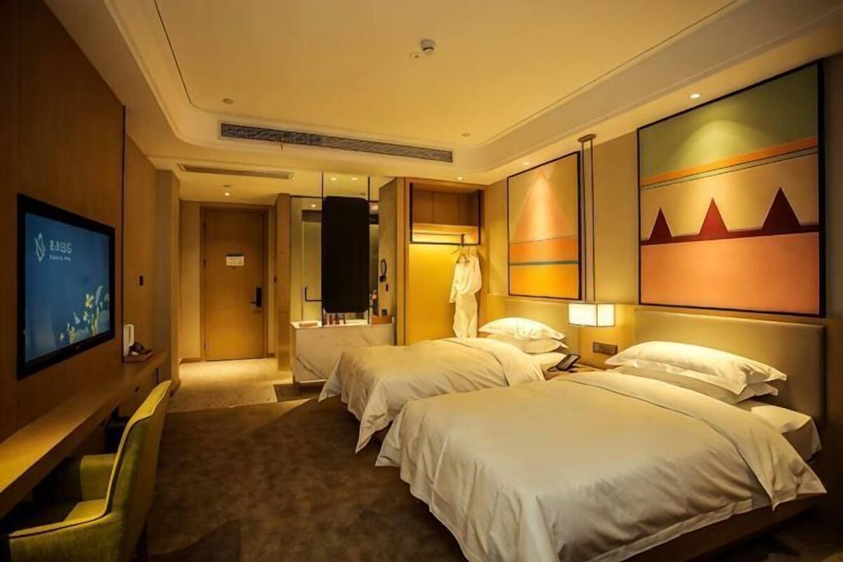 A hotel room with two beds, a TV, a desk, and a large painting on the wall.