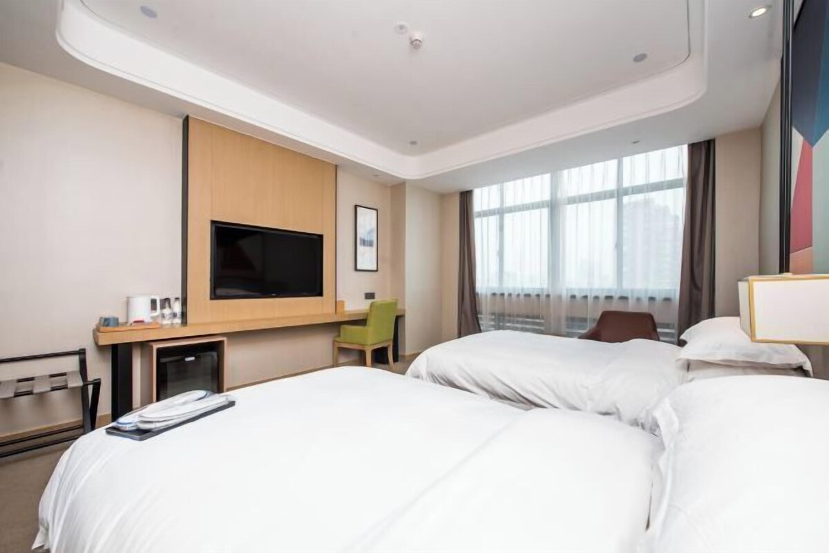 Habitación de hotel con dos camas, un escritorio, un televisor y una ventana con cortinas.