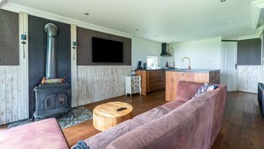 A modern living room with a large sofa, a round wooden coffee table, a built-in wood stove, and a kitchen area with a sink and countertop.