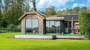 A modern house with large glass windows, a green lawn, and a solar panel on the roof.