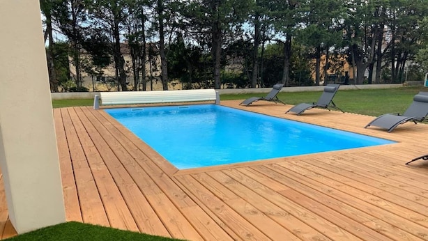 Una piscina con muelle de madera y borde de césped, rodeada de árboles.