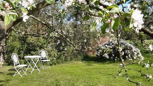 Un jardin avec une pelouse, une clôture en bois et deux chaises en métal blanc.