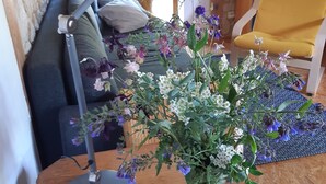 Une pièce avec une table en bois, une lampe de bureau, un canapé, une chaise jaune et une fenêtre avec des rideaux.