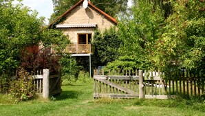 Une maison de campagne avec un balcon, entourée d’une végétation luxuriante et d’une clôture en bois.