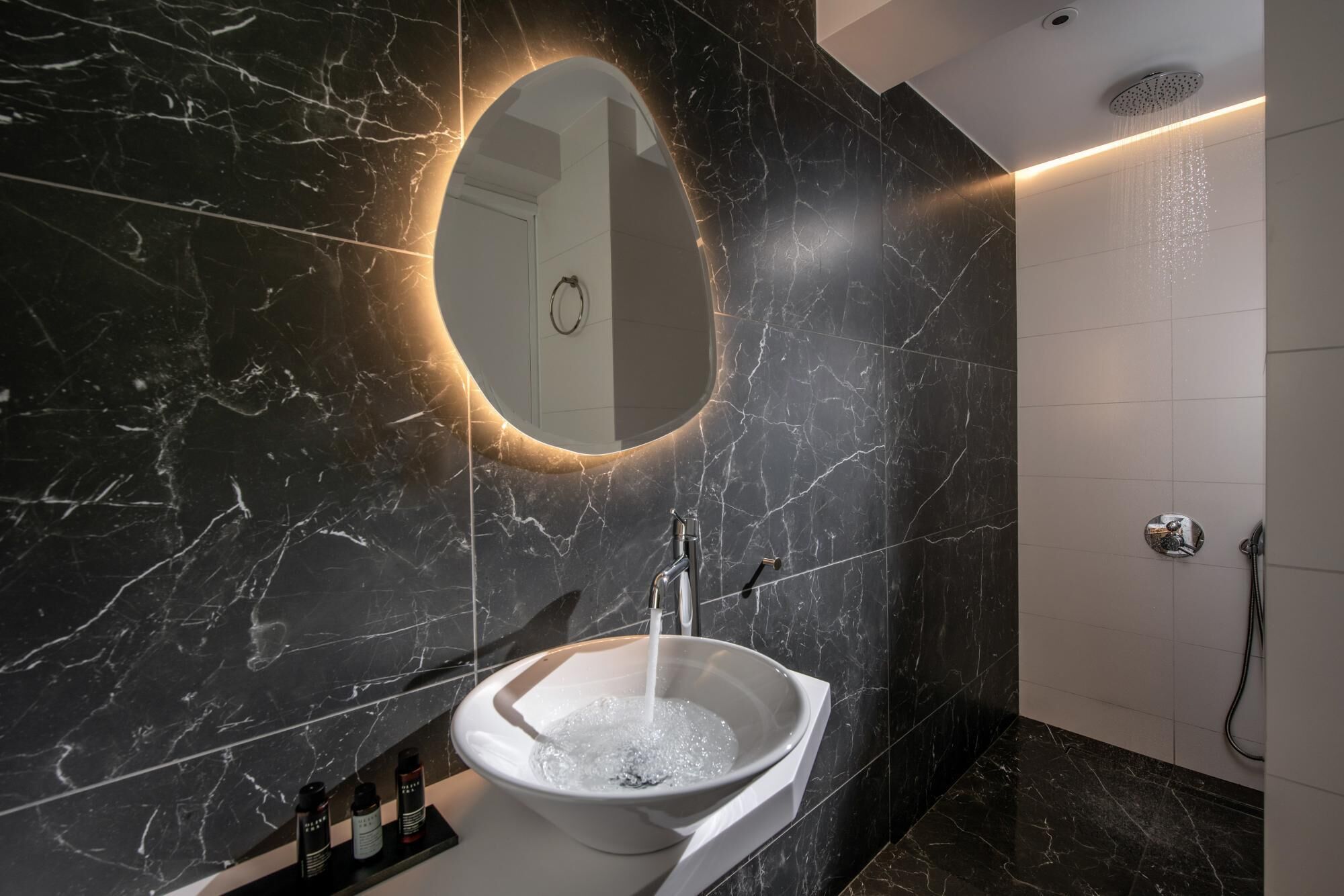 Une salle de bain moderne avec un lavabo en marbre, un miroir rond et un espace douche.