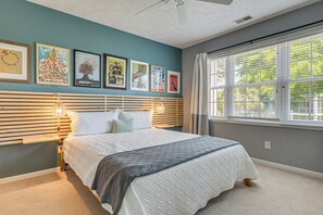 Une chambre à coucher avec un lit, une fenêtre avec des stores et des œuvres d’art murales.