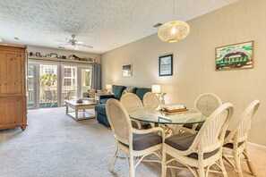 Un coin repas avec une table en verre et des chaises en osier, un ventilateur de plafond et une vue sur un balcon extérieur, accessible par des portes vitrées.